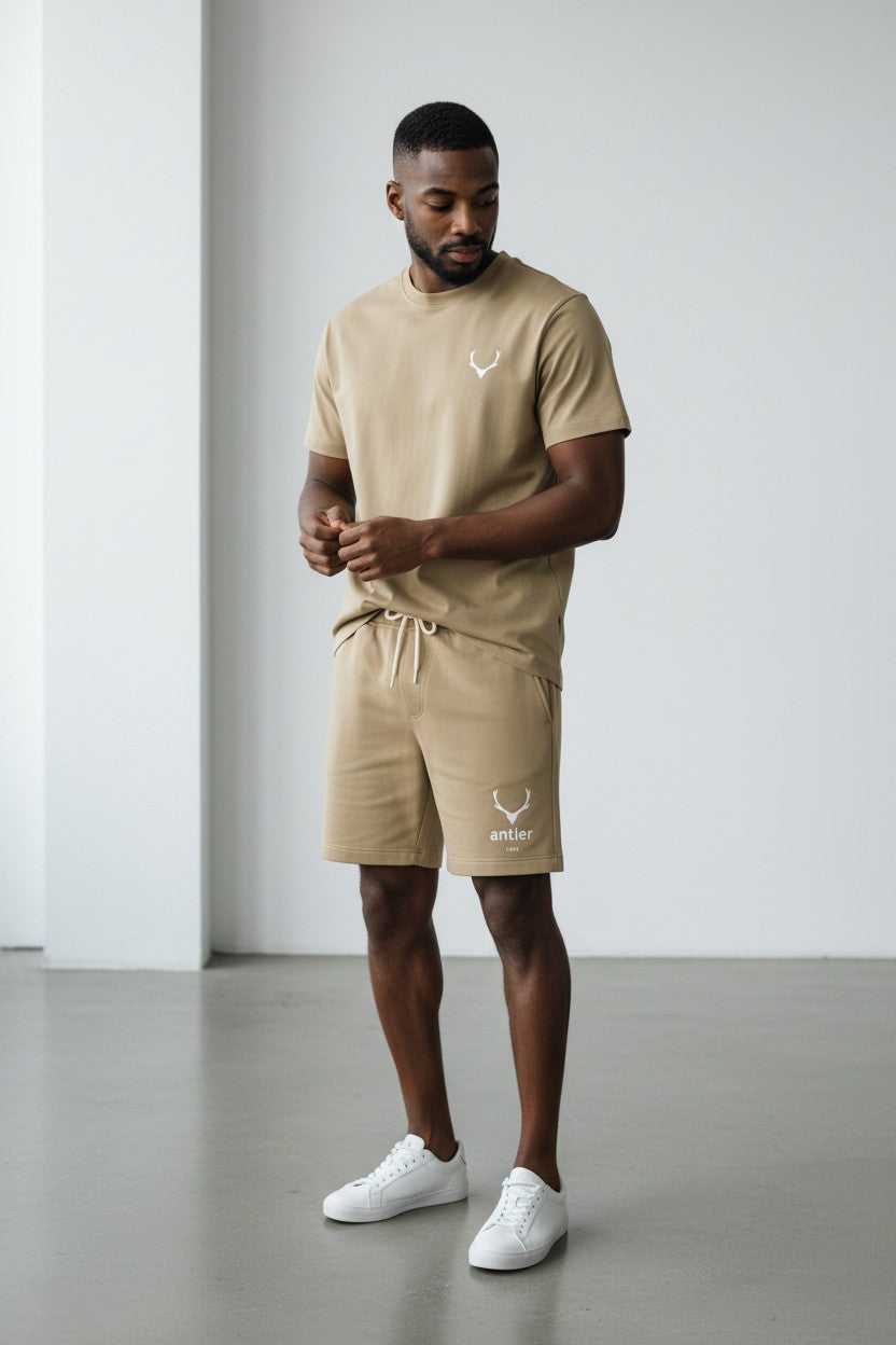Man wearing a beige t-shirt and shorts set with a logo, standing against a plain background. Antler, Monza Outlet, Monza Fashion, Shein Outlet