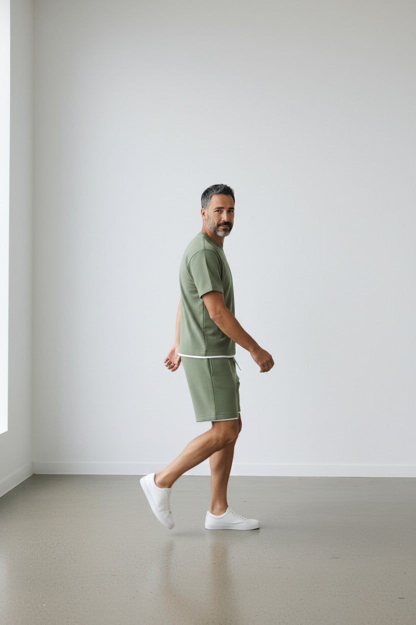 Man in a green outfit walking in a minimalistic room with white walls and gray floor.