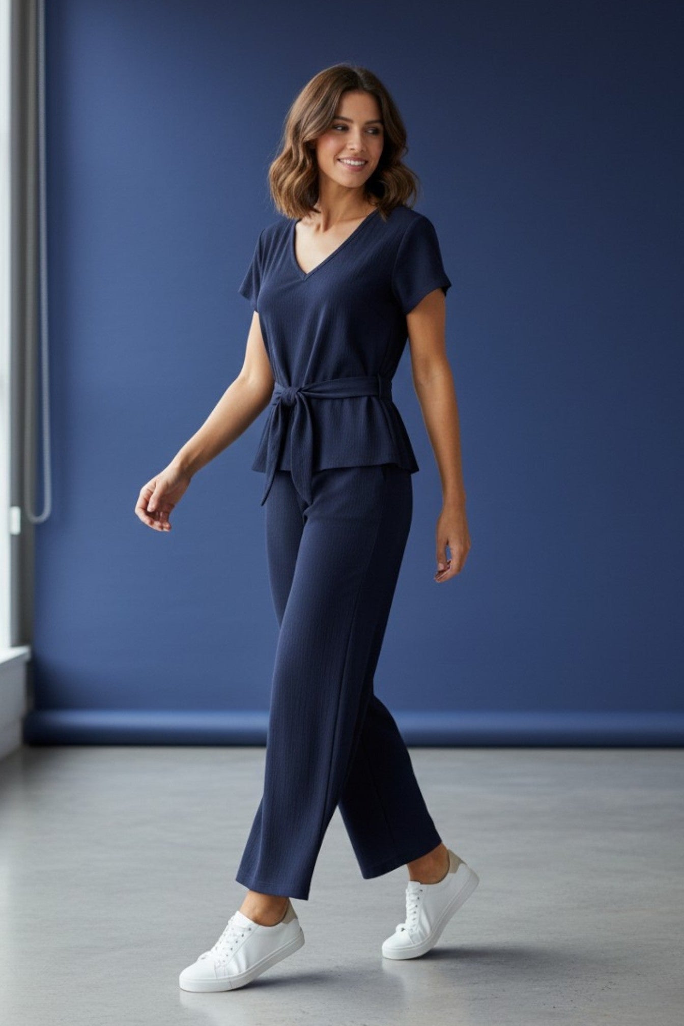 Woman wearing a navy blue outfit with white sneakers against a blue wall. Antler, Monza Outlet, Monza Fashion, Shein Outlet
