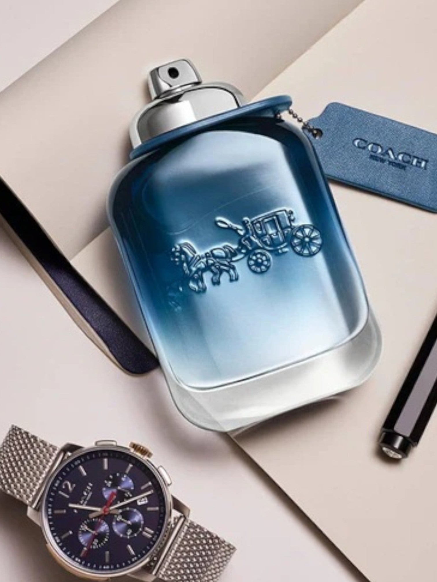 Blue perfume bottle with Coach logo, watch, and pen on a light background. Coach, Monza Outlet, Monza Fashion, Shein Outlet