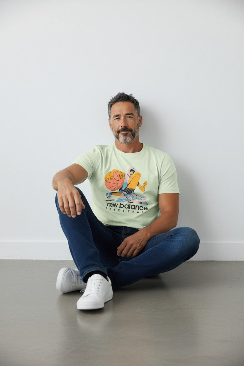 Man sitting on the floor wearing a light green t-shirt with a colorful graphic and text. New Balance, Monza Outlet, Monza Fashion, Shein Outlet
