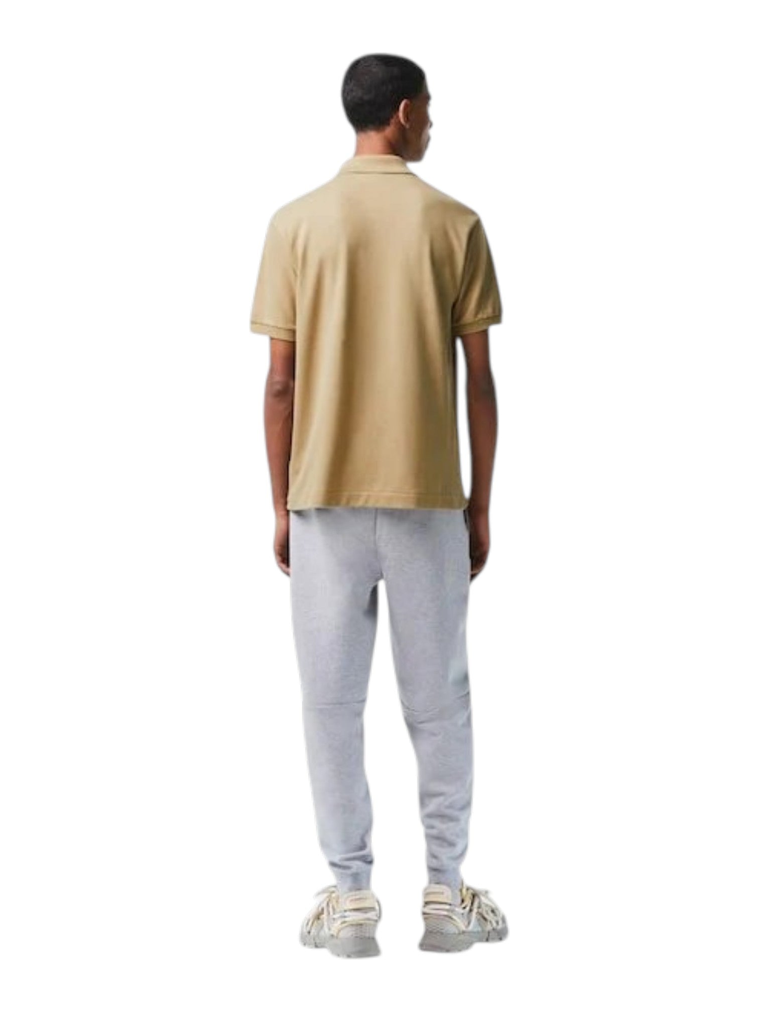 Person wearing a beige polo shirt and light gray pants on a white background. Lacoste, Monza Outlet, Monza Fashion, Shein Outlet
