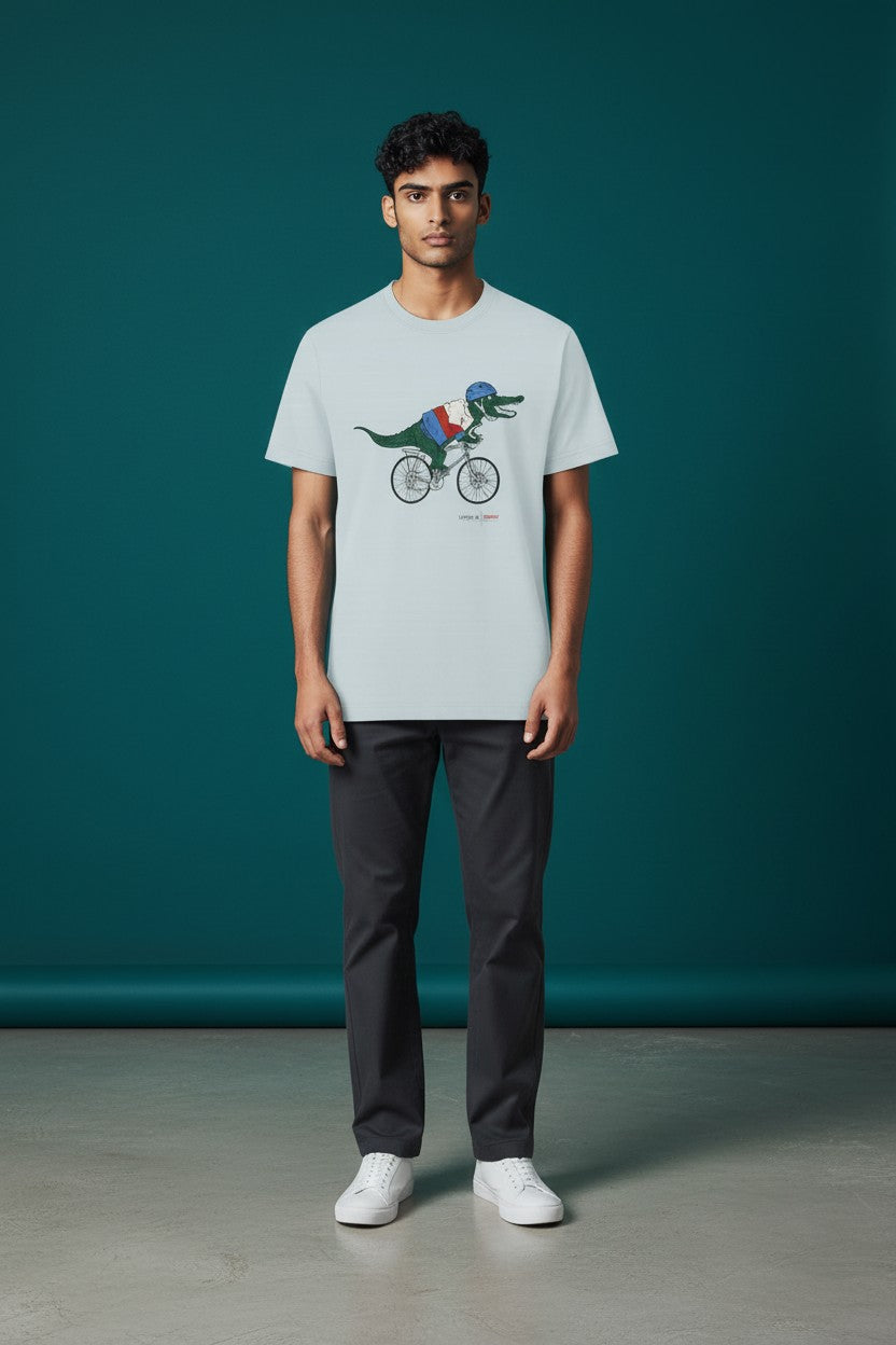 Person wearing a t-shirt with a graphic design of a dinosaur on a bicycle against a teal background. Lacoste, Monza Outlet, Monza Fashion, Shein Outlet