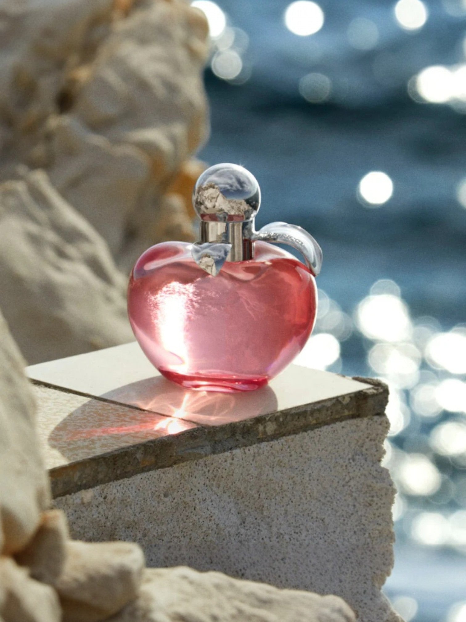 Pink perfume bottle with silver cap on a stone ledge by water. Nina, Monza Outlet, Monza Fashion, Shein Outlet