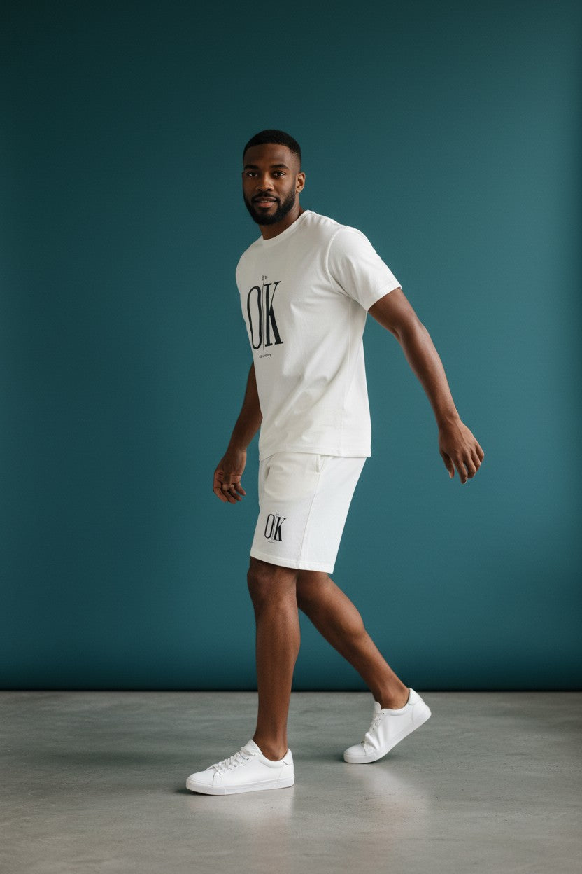 Man wearing a white t-shirt and shorts with OK branding against a teal background. Antler, Monza Outlet, Monza Fashion, Shein Outlet