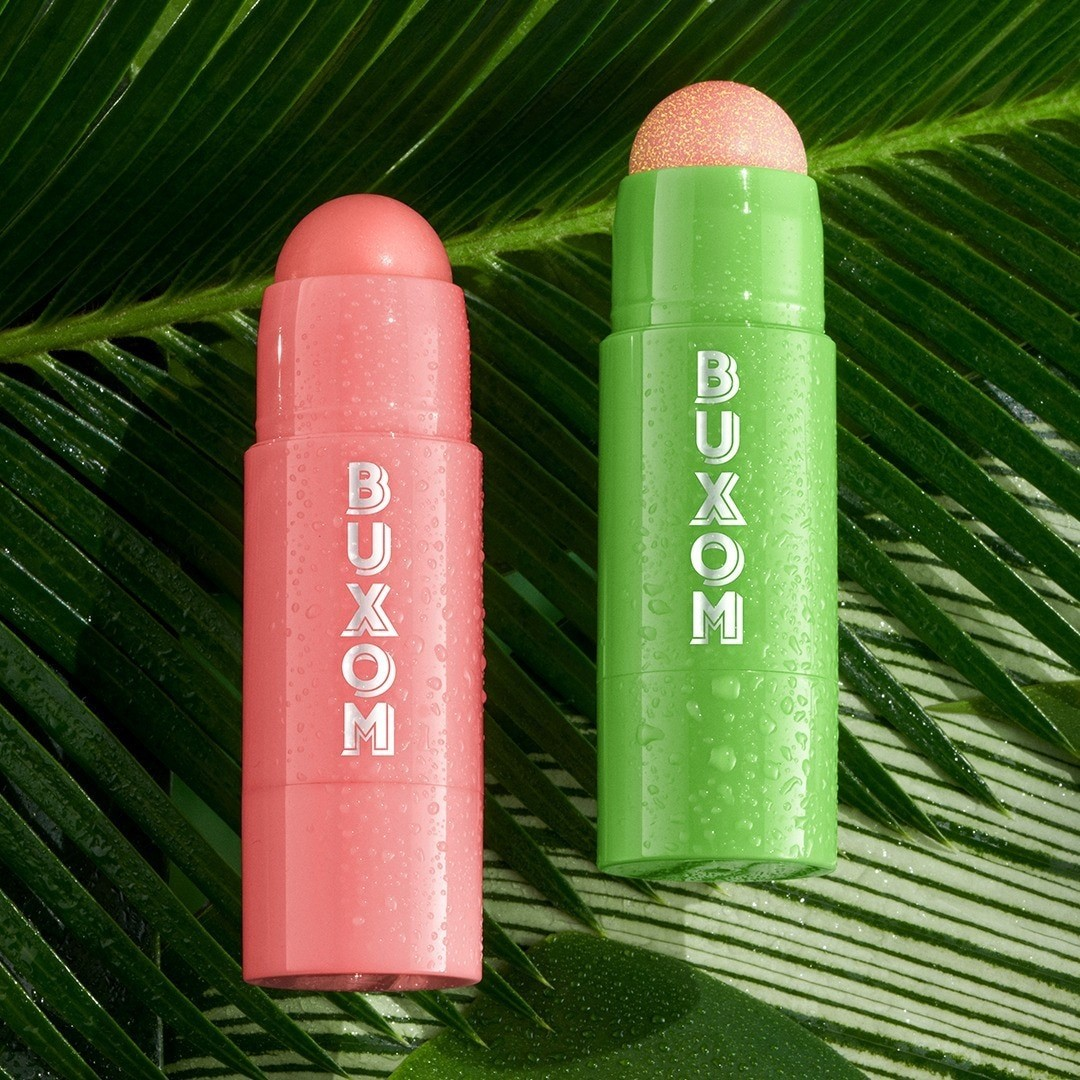 Two Buxom makeup sticks, one pink and one green, on a leaf background. Monza Outlet
