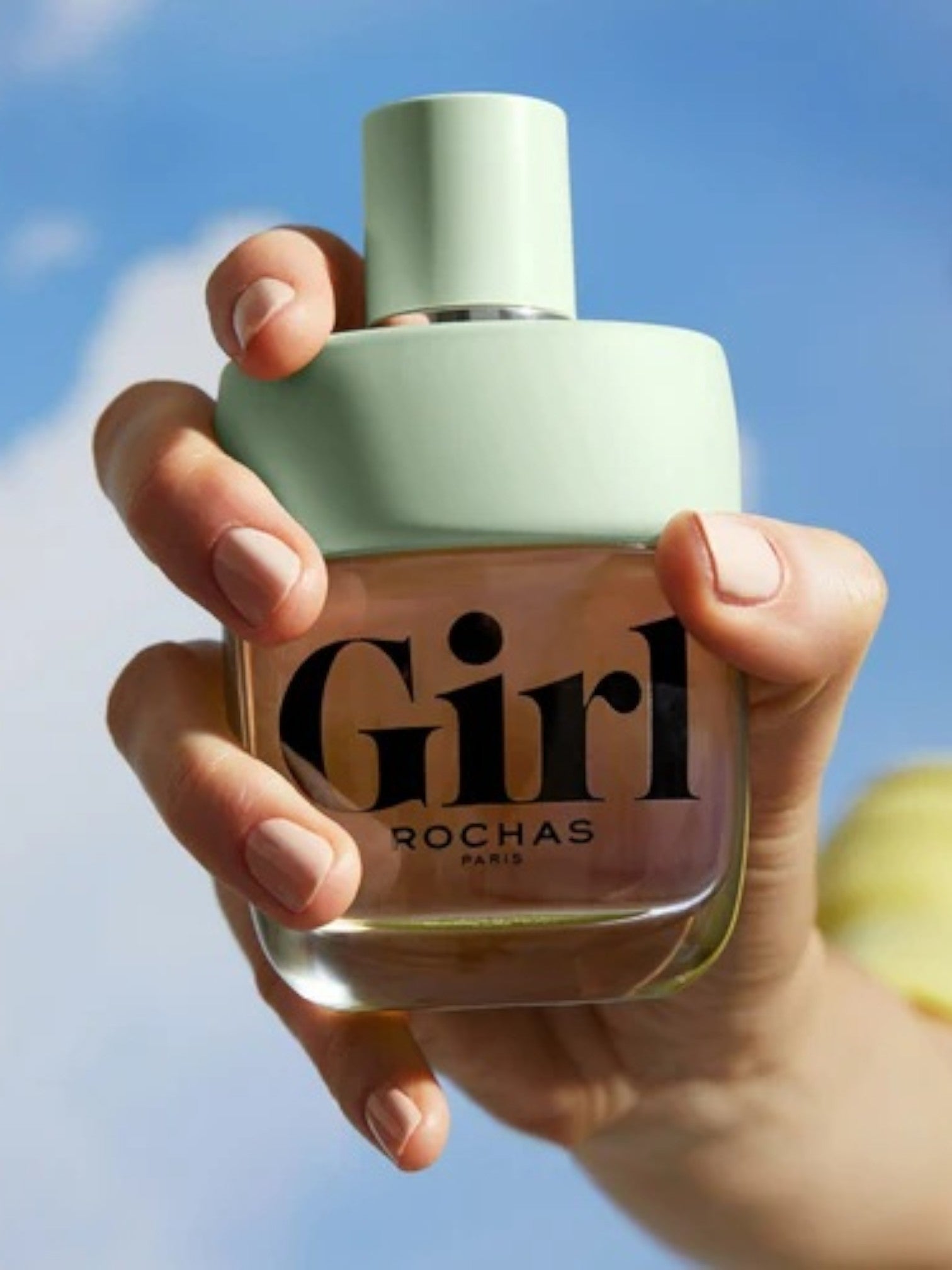 Hand holding a Rochas Girl perfume bottle against a blue sky. Rochas, Monza Outlet, Monza Fashion, Shein Outlet