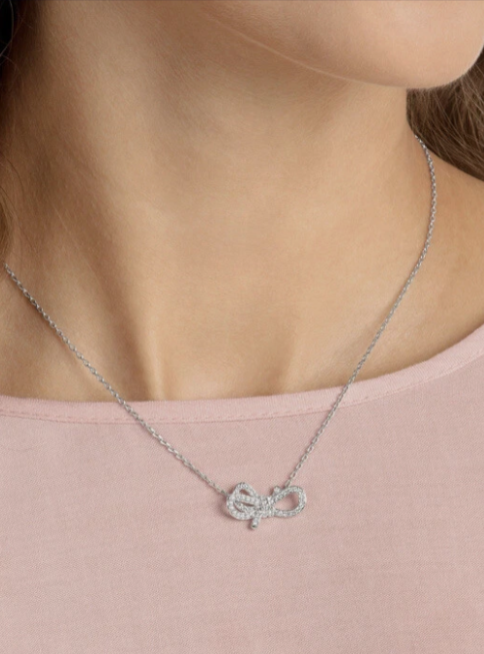 Necklace with a bow-shaped pendant worn by a person on a plain background. Swarovski Monza Outlet