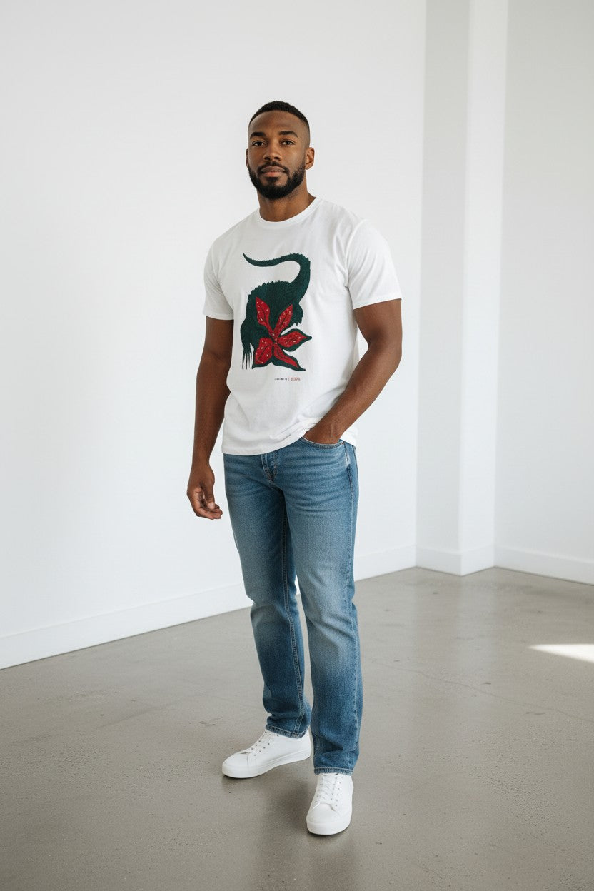 Man wearing a white t-shirt with a graphic design, blue jeans, and white sneakers in a minimalistic setting. Lacoste, Monza Outlet, Monza Fashion, Shein Outlet