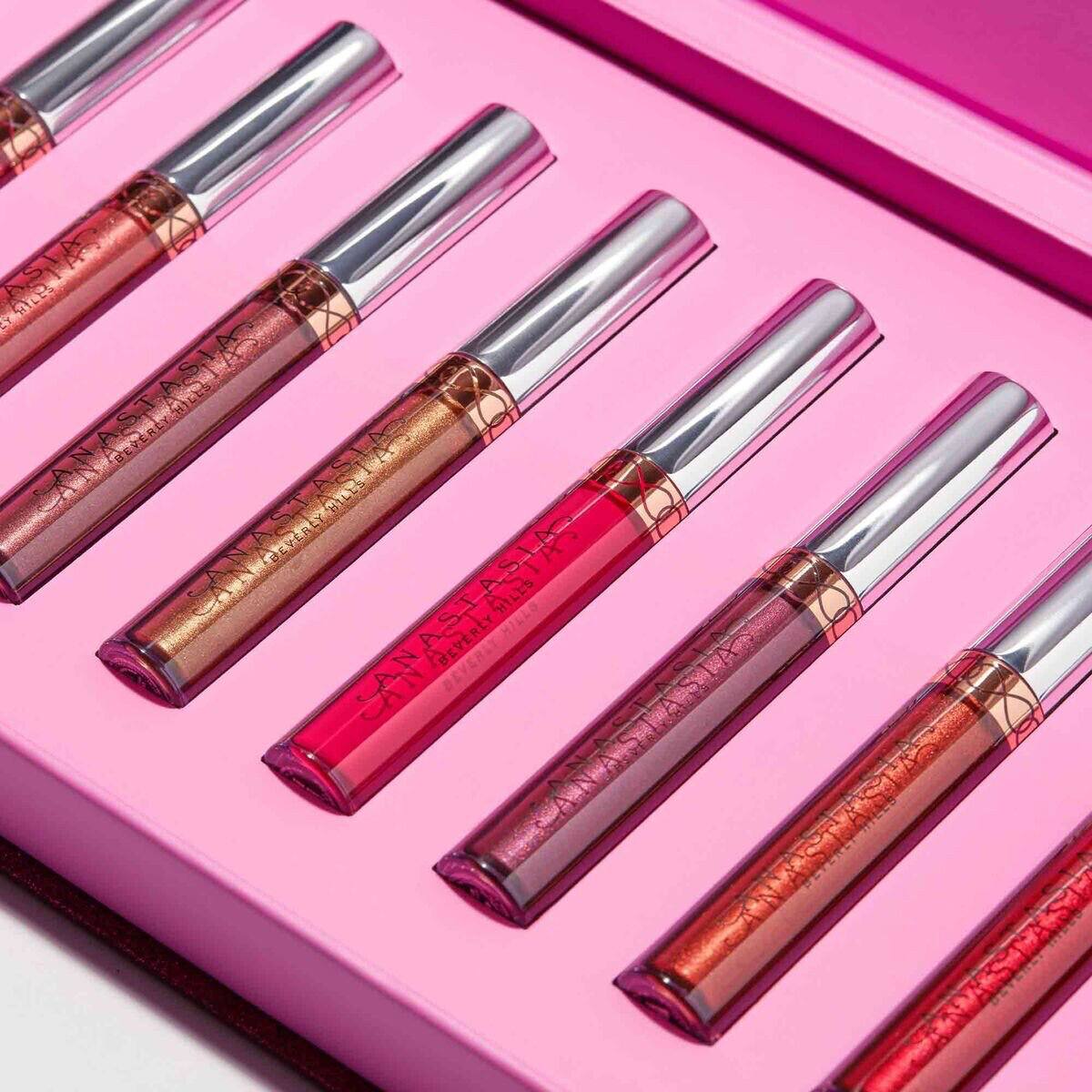 Set of lip glosses with metallic and glossy finishes on a pink background Monza fashion outlet, monza outlet, shein outlet, shien outlet cosmetics, makeup, perfume
