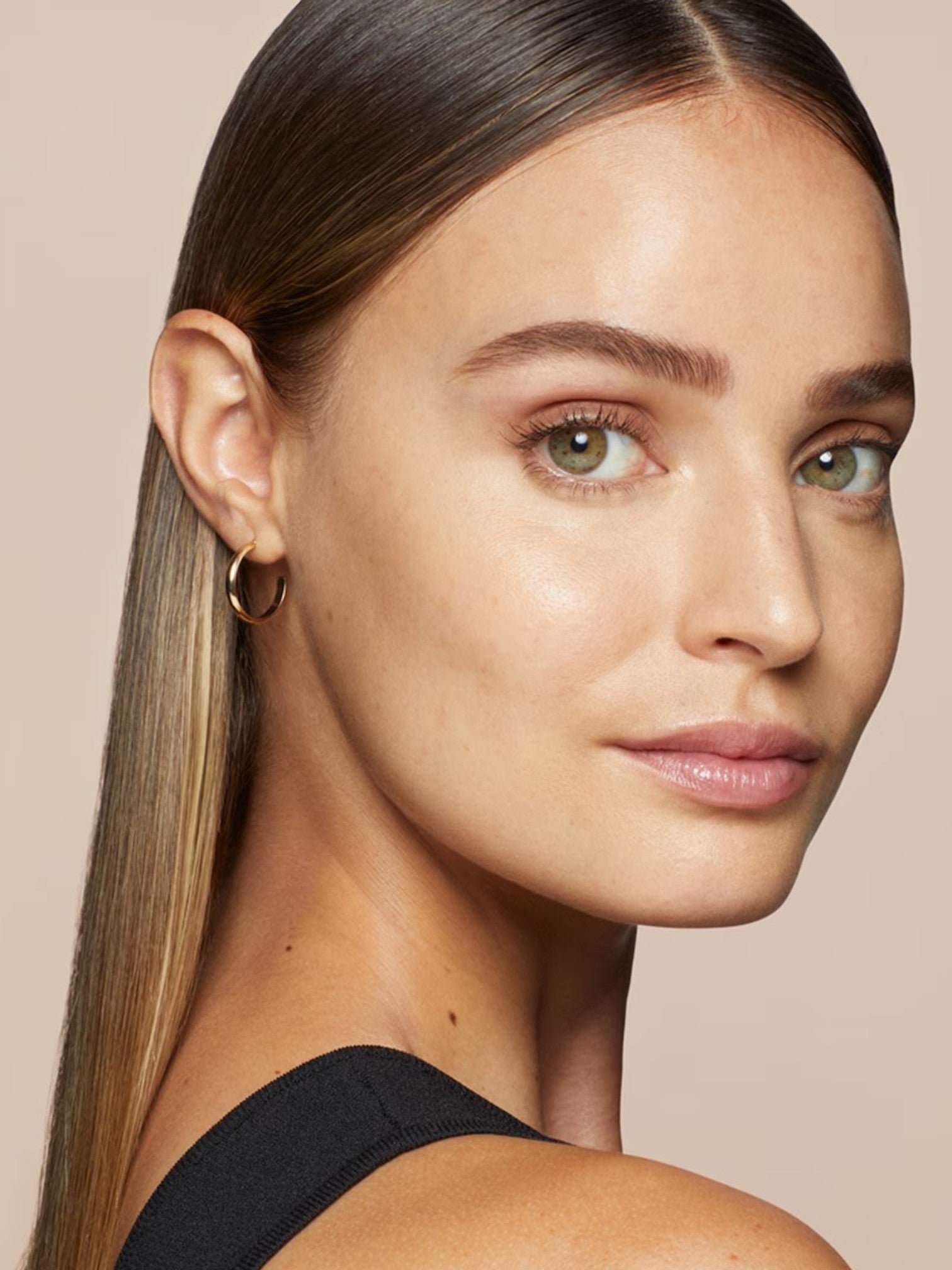 Close-up of a woman with a gold hoop earring against a beige background. Bobbi Brown, Monza Outlet, Monza Fashion, Shein Outlet