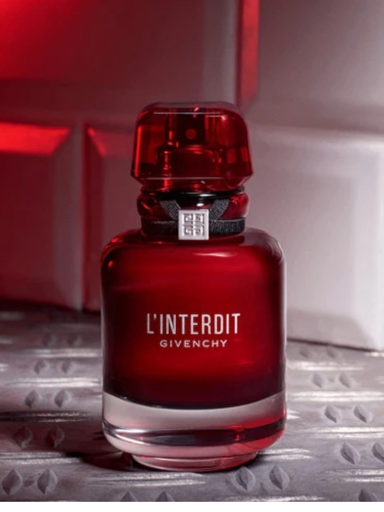 Red Givenchy L'Interdit perfume bottle on a metallic surface with a red background monza outlet, Shein outlet, monza fashion