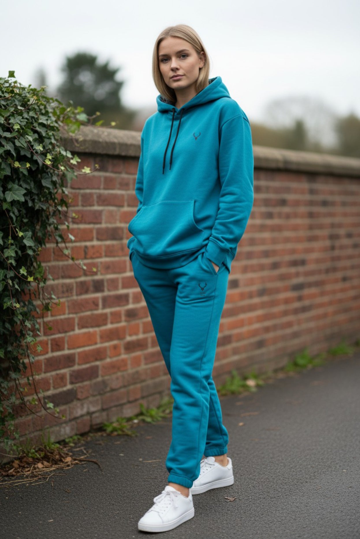 Person wearing a blue tracksuit standing against a brick wall. Antler, Monza Outlet, Monza Fashion, Shein Outlet