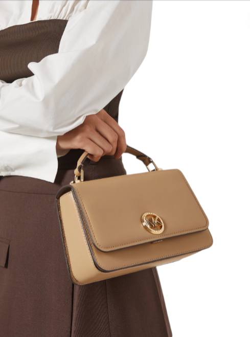 Beige handbag with gold clasp held by a person wearing a white shirt and brown pants.