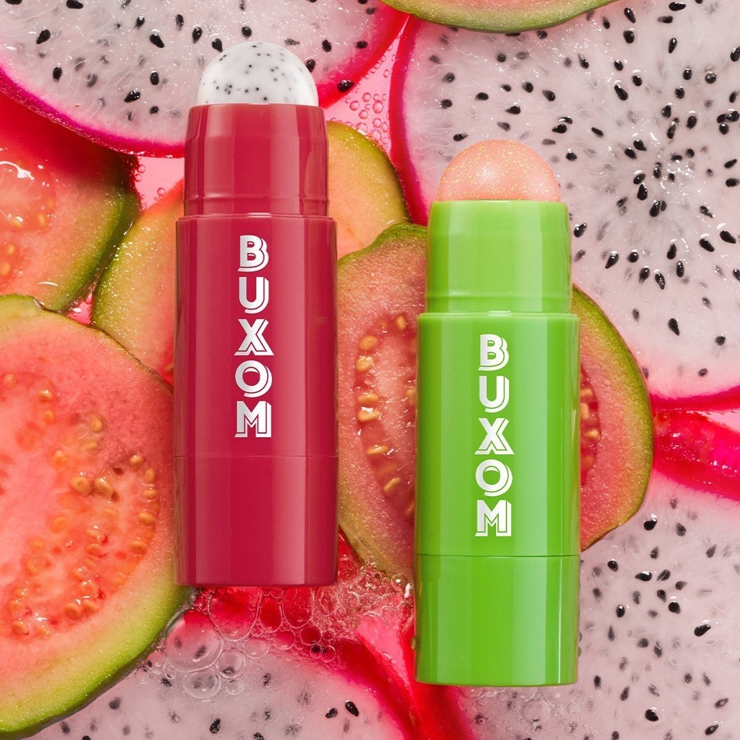 Two Buxom lip balm sticks, one red and one green, on a background of sliced dragon fruit. Monza Outlet