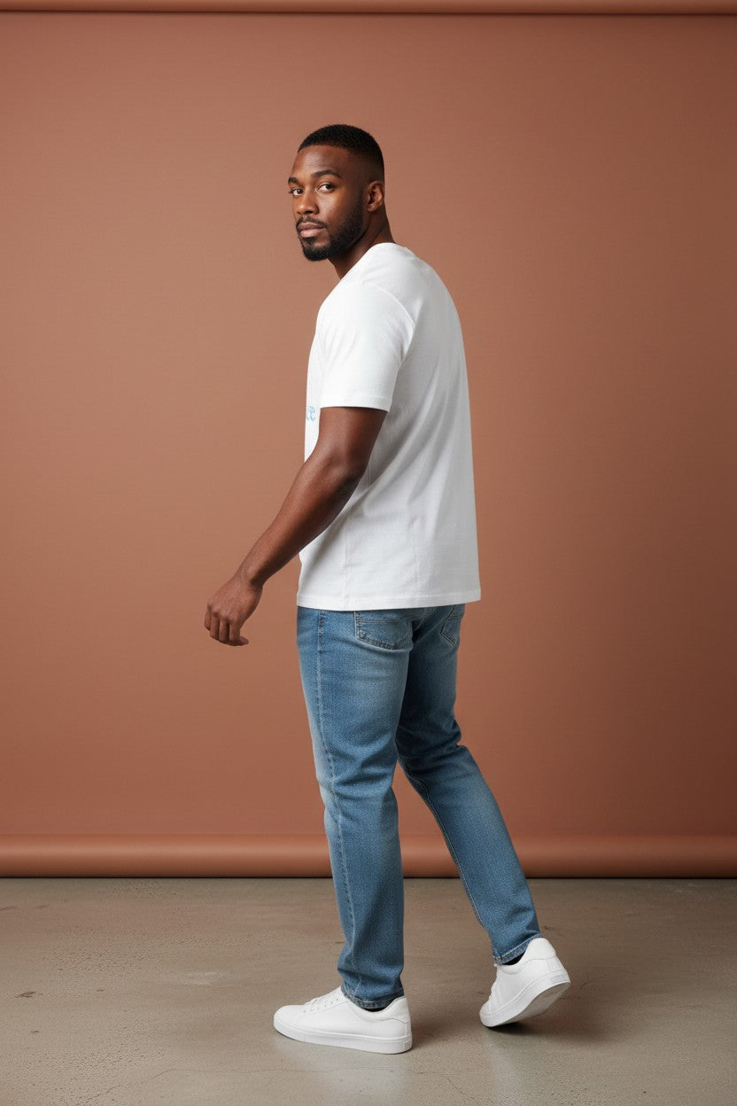 Man wearing a white t-shirt, blue jeans, and white sneakers against a brown background. New Balance, Monza Outlet, Monza Fashion, Shein Outlet