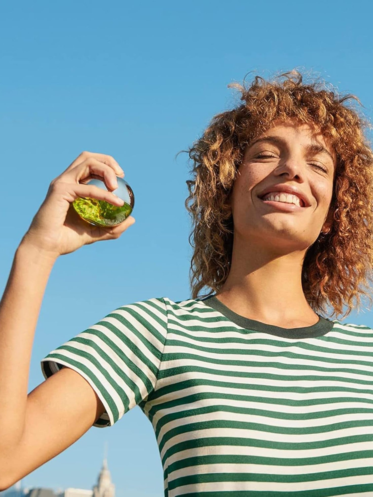 Woman holding a glass of green liquid against a blue sky. Dkny, Monza Outlet, Monza Fashion, Shein Outlet