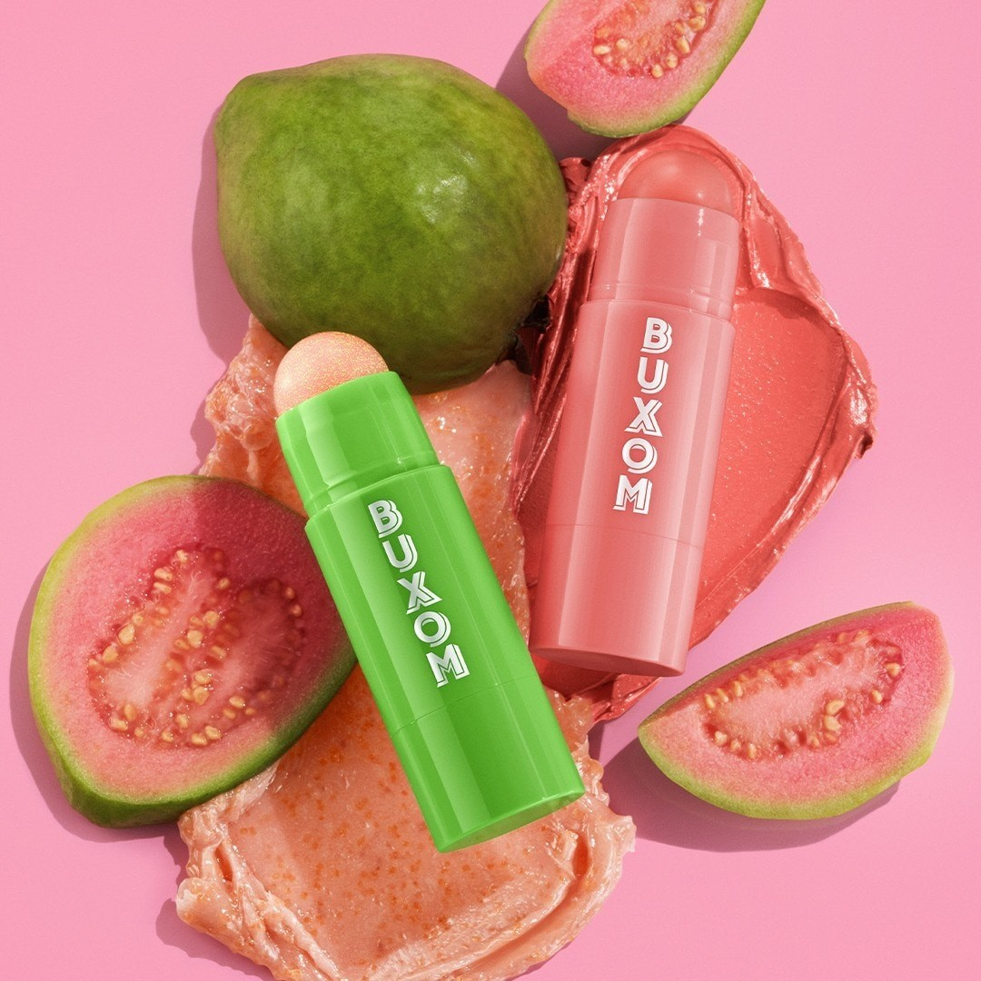 Two Buxom lip products on a pink background with guava slices. Monza Outlet