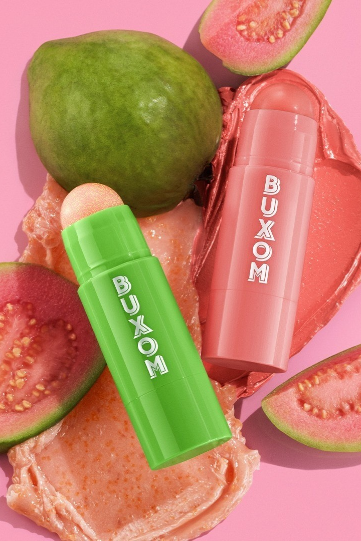 Two Buxom lip products on a pink background with guava slices. Monza Outlet