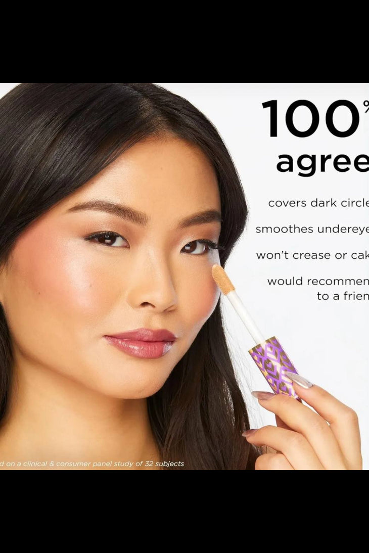 Woman applying concealer with a brush, product labeled '100% agree', on a white background. Monza fashion outlet, monza outlet, shein outlet, shien outlet cosmetics, makeup, perfume