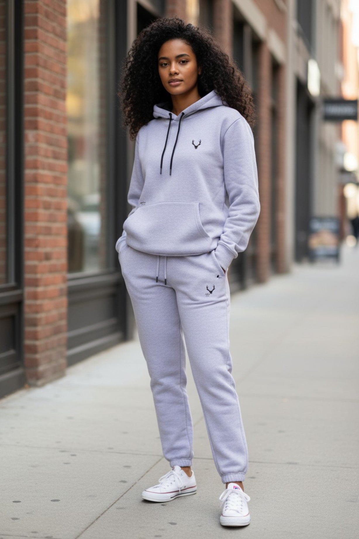 Person wearing a gray hoodie and pants with a logo on a city street. Antler, Monza Outlet, Monza Fashion, Shein Outlet