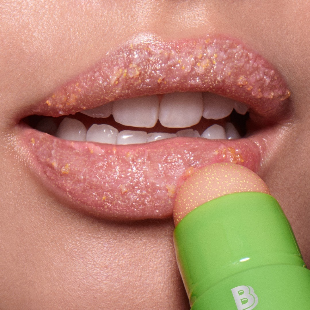 Close-up of a person applying a lip scrub with a green applicator. Monza fashion outlet, monza outlet, shein outlet, shien outlet cosmetics, makeup, perfume