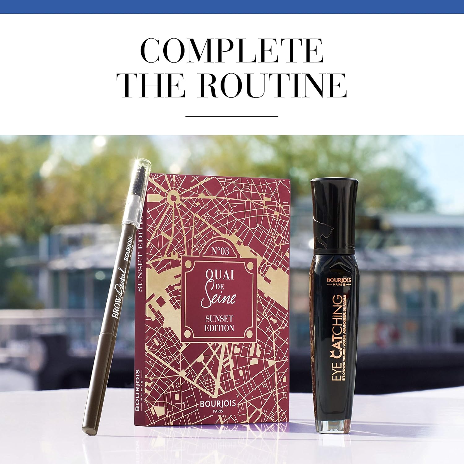 Bourjois makeup products including a pen, a box with a map design, and a bottle of perfume on a blurred outdoor background. Monza Outlet