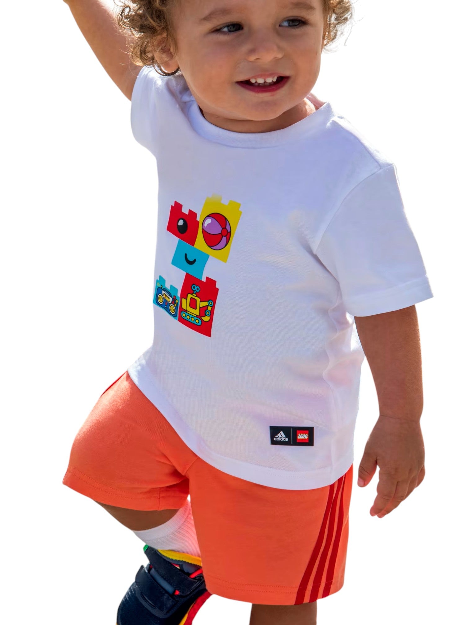 Child wearing a white t-shirt with colorful graphics and orange shorts on a white background. Adidas, Monza Outlet, Monza Fashion, Shein Outlet