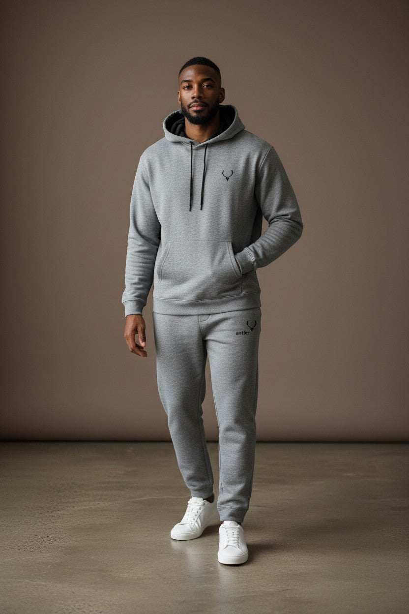 Man wearing a gray hoodie and jogger set with white sneakers against a brown background. Antler, Monza Outlet, Monza Fashion, Shein Outlet