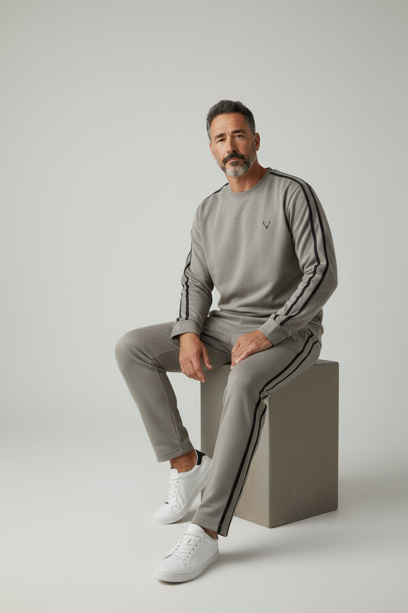 Man wearing a gray tracksuit with black stripes sitting on a beige cube against a light gray background. Antler, Monza Outlet, Monza Fashion, Shein Outlet
