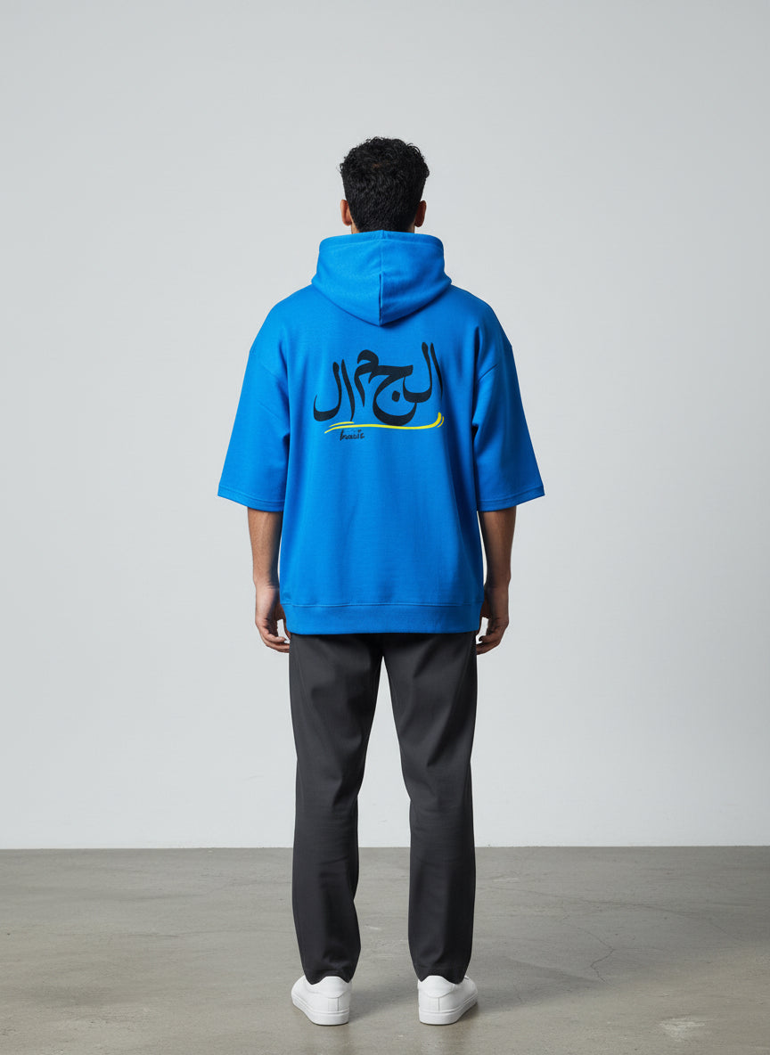 Person wearing a blue hoodie with Arabic text on the back, standing against a plain background. Antler, Monza Outlet, Monza Fashion, Shein Outlet  