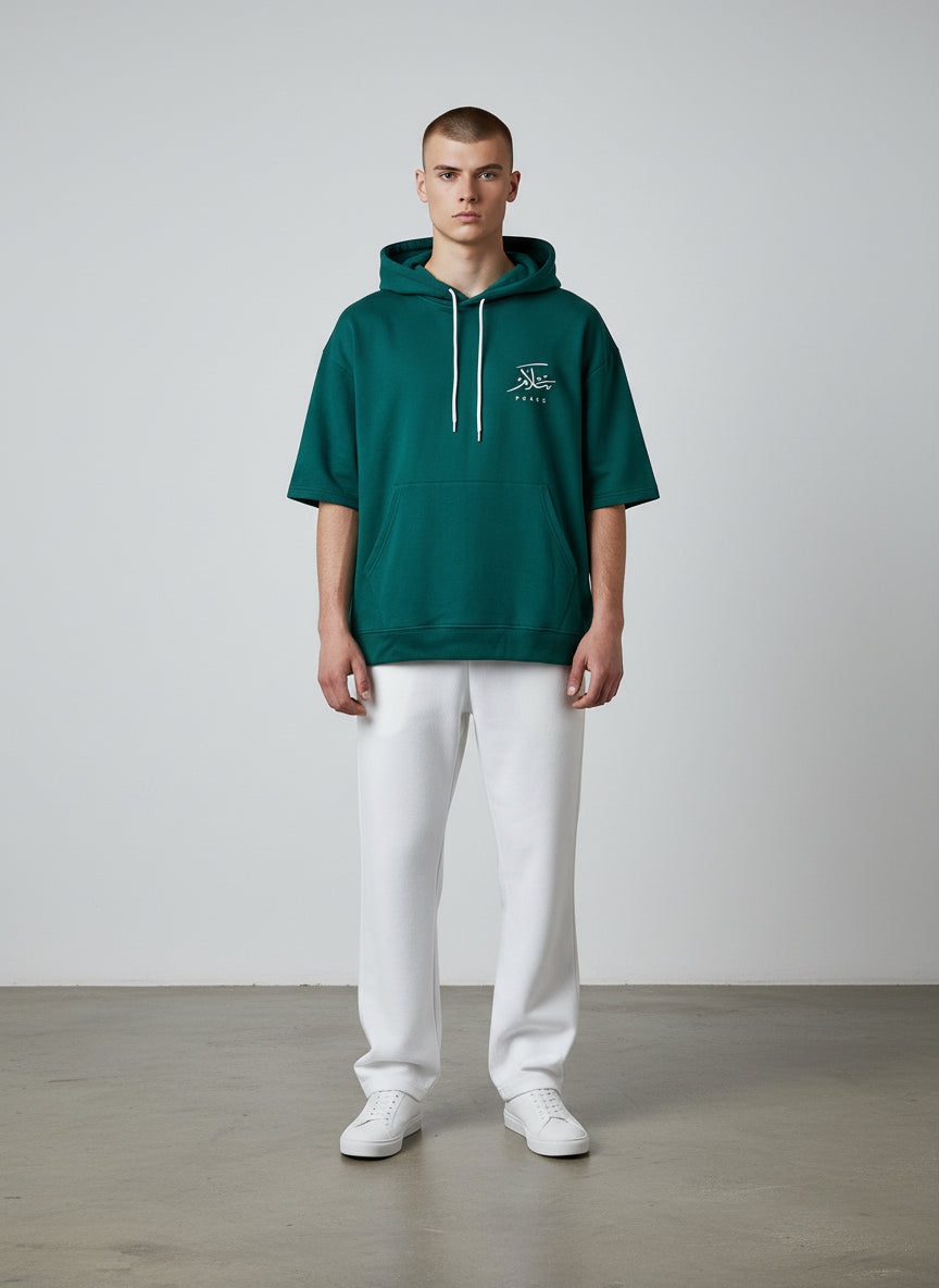 Person wearing a green hoodie with a logo and white pants on a plain background. Antler, Monza Outlet, Monza Fashion, Shein Outlet  
