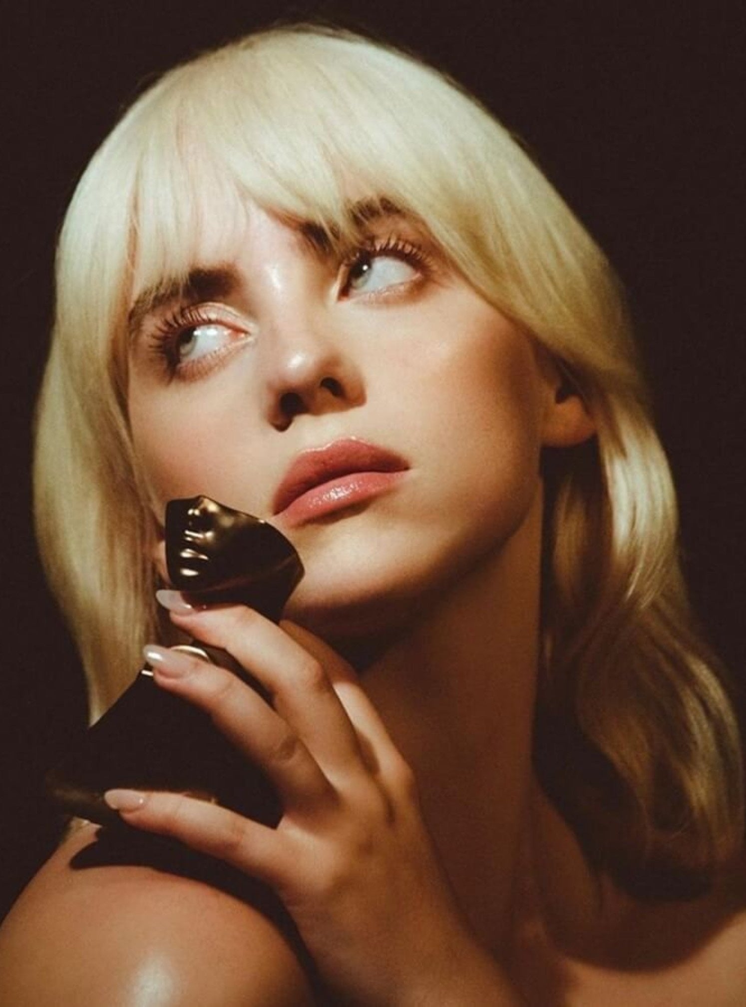 Woman holding a black object close to her face against a dark background. Billie Eilish, Monza Outlet, Monza Fashion, Shein Outlet