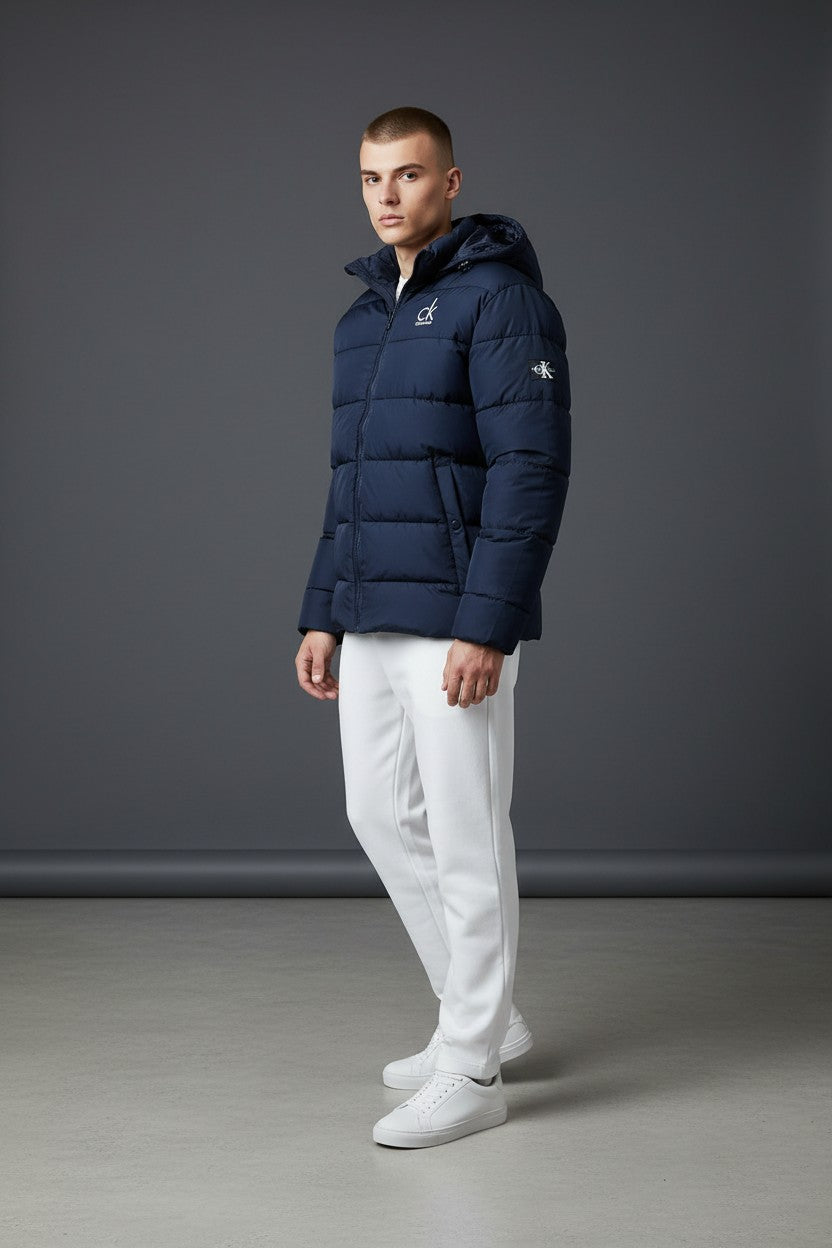 Man wearing a navy blue puffer jacket with a logo on a gray background. Calvin Klein, Monza Outlet, Monza Fashion, Shein Outlet