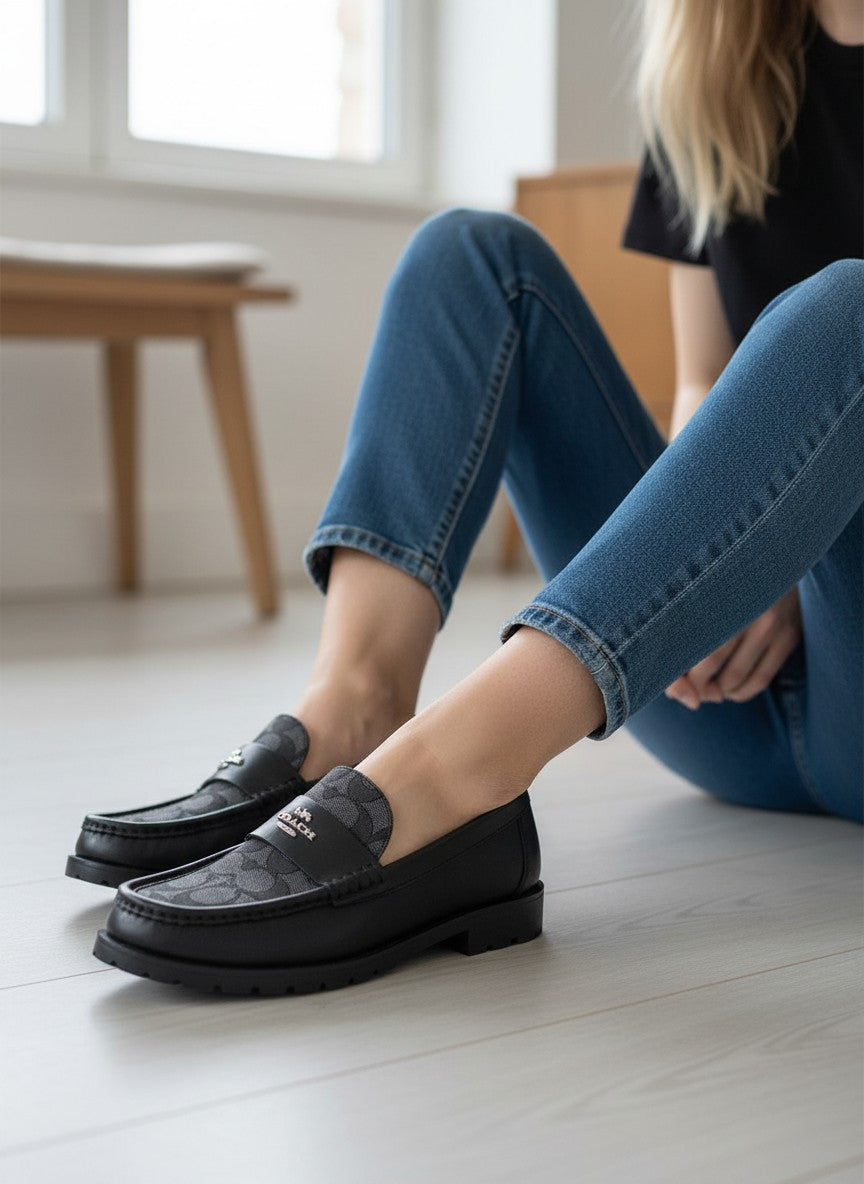 Person wearing black loafers and blue jeans sitting on a light wood floor. Coach, Monza Outlet, Monza Fashion, Shein Outlet 