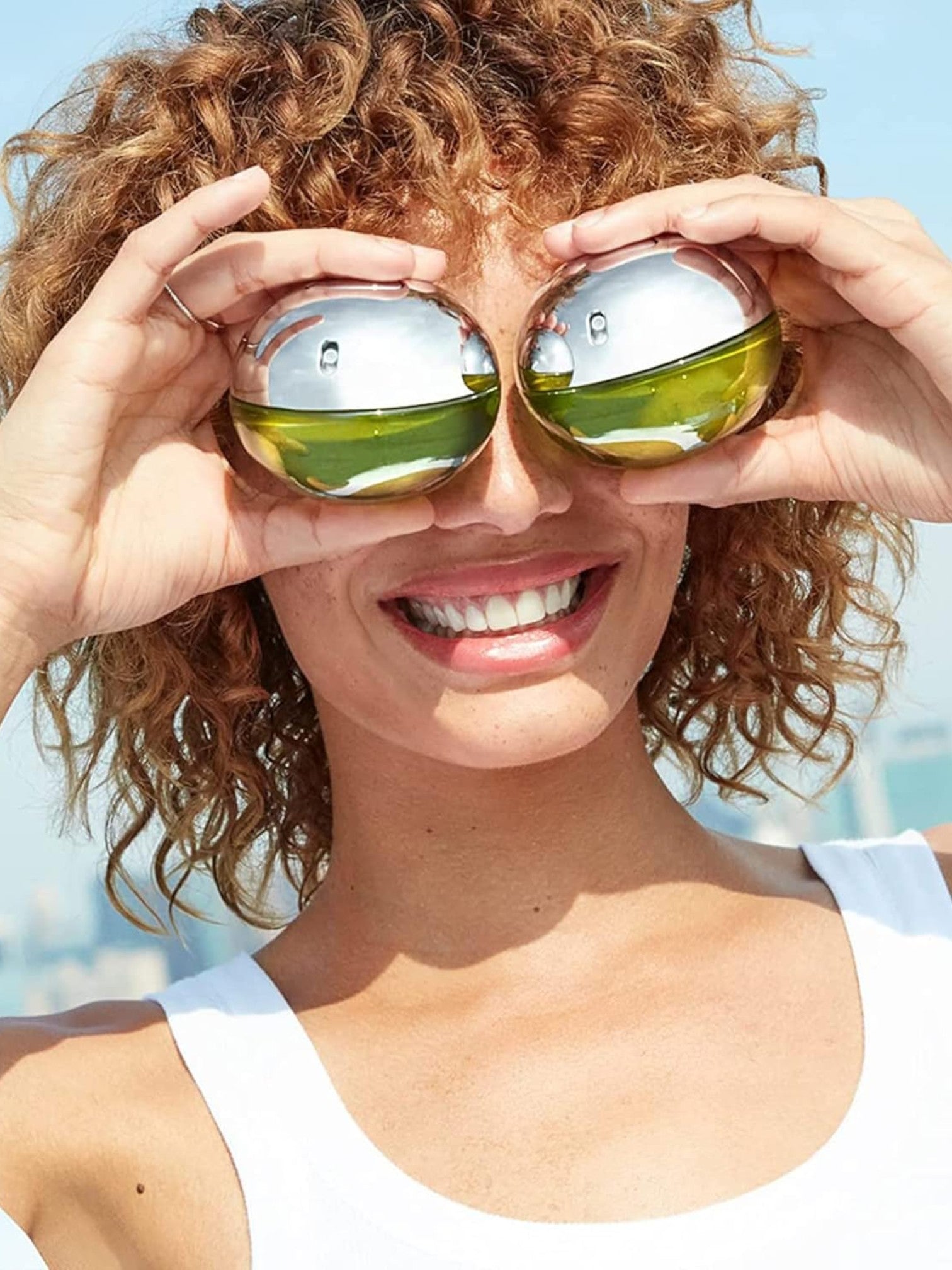 Person holding green bottles with reflective silver tops over their eyes against a clear blue sky. Calvin Klein, Monza Outlet, Monza Fashion, Shein Outlet