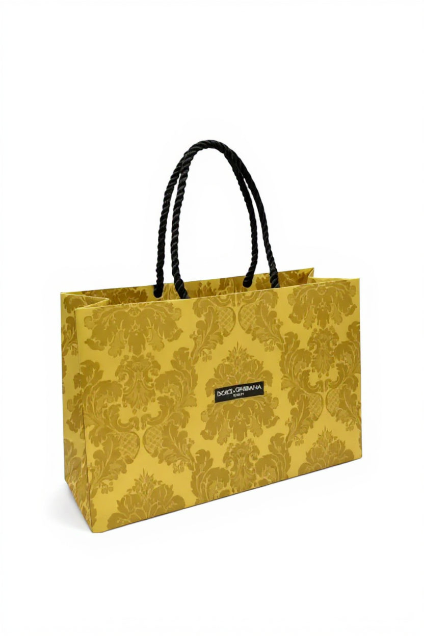 Yellow floral-patterned paper bag with black handle on a white background. Dolce & Gabbana, Monza Outlet, Monza Fashion, Shein Outlet