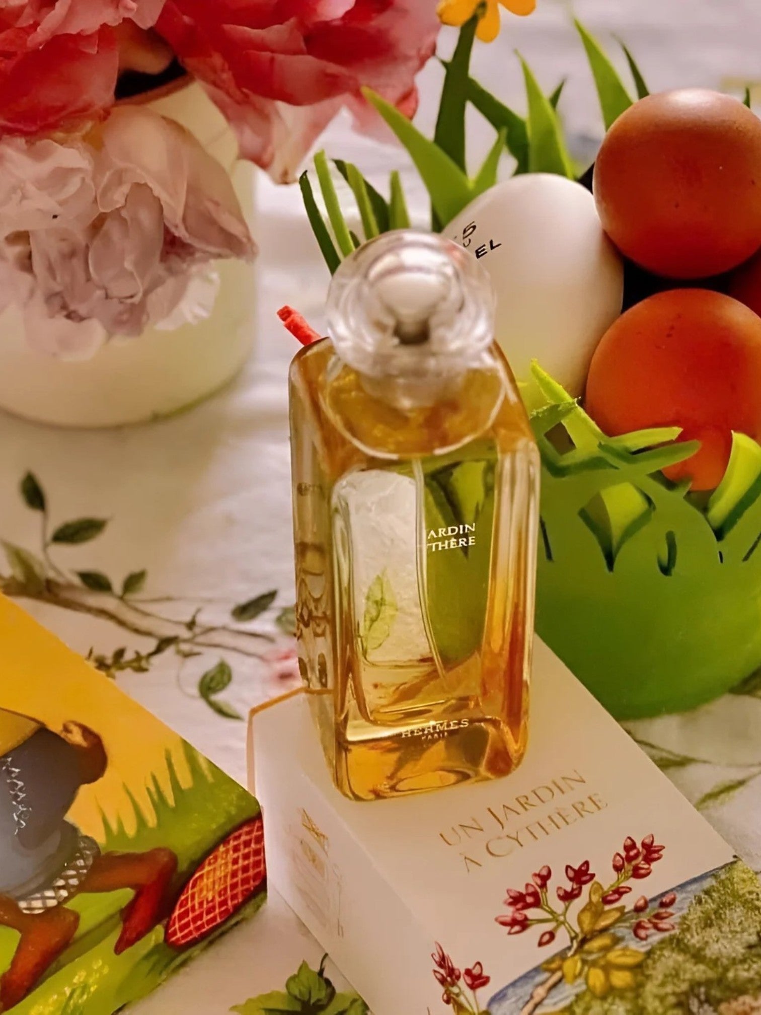 Perfume bottle labeled Un Jardin a Citee on a decorative box with flowers and fruits in the background. Hermes, Monza Outlet, Monza Fashion, Shein Outlet