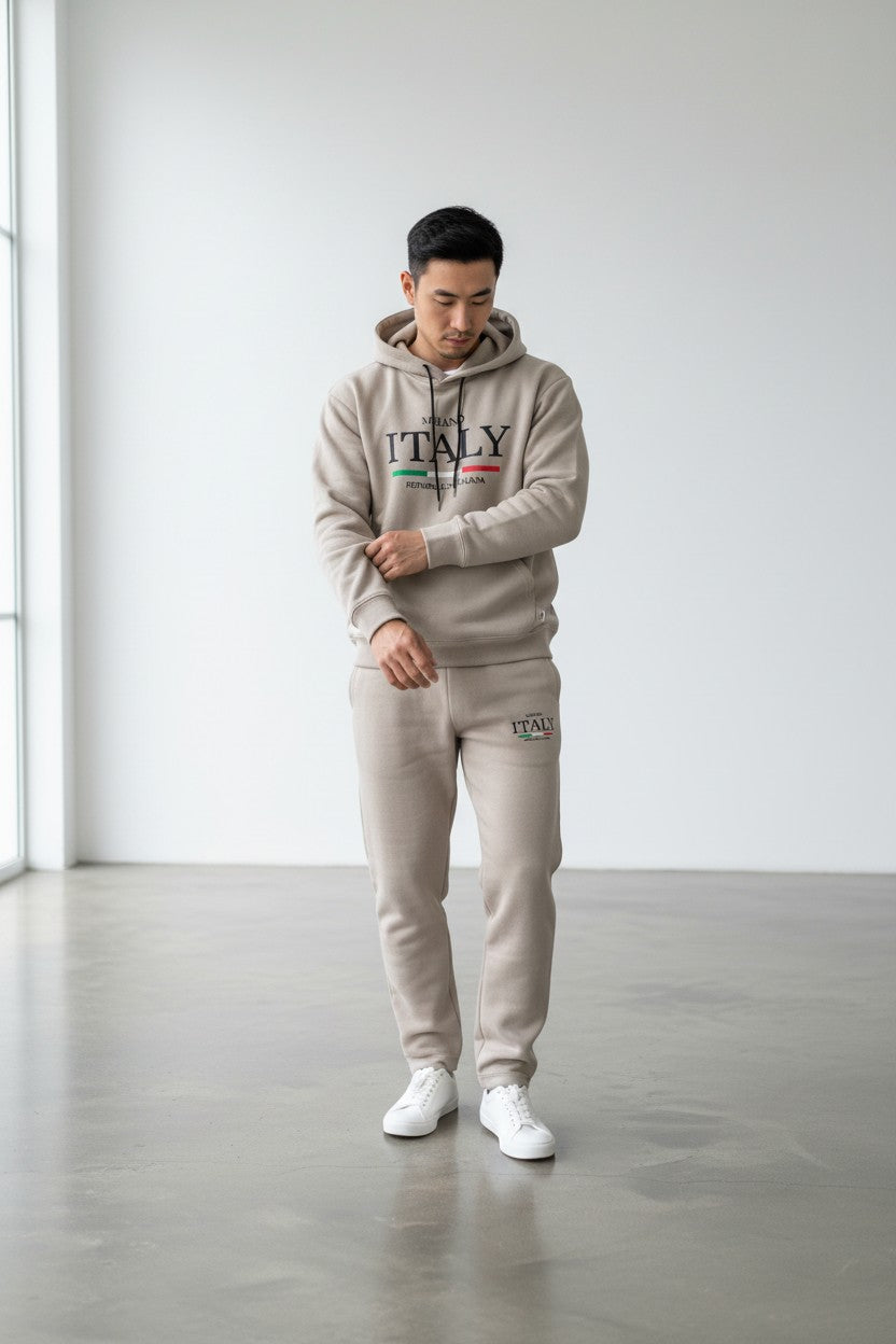 Person wearing a beige ITALY hoodie and pants in a minimalistic setting. Antler, Monza Outlet, Monza Fashion, Shein Outlet