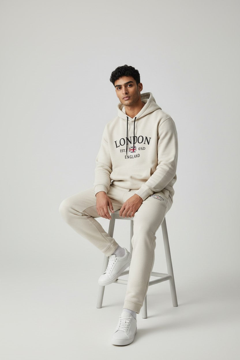 Man sitting on a stool wearing a cream hoodie with text and matching pants on a light gray background. Antler, Monza Outlet, Monza Fashion, Shein Outlet