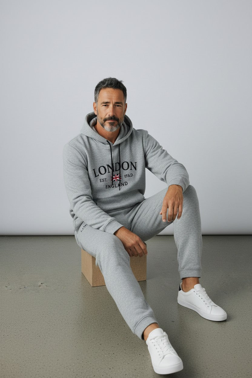 Man wearing a gray London hoodie and pants sitting on a box against a plain background. Antler, Monza Outlet, Monza Fashion, Shein Outlet