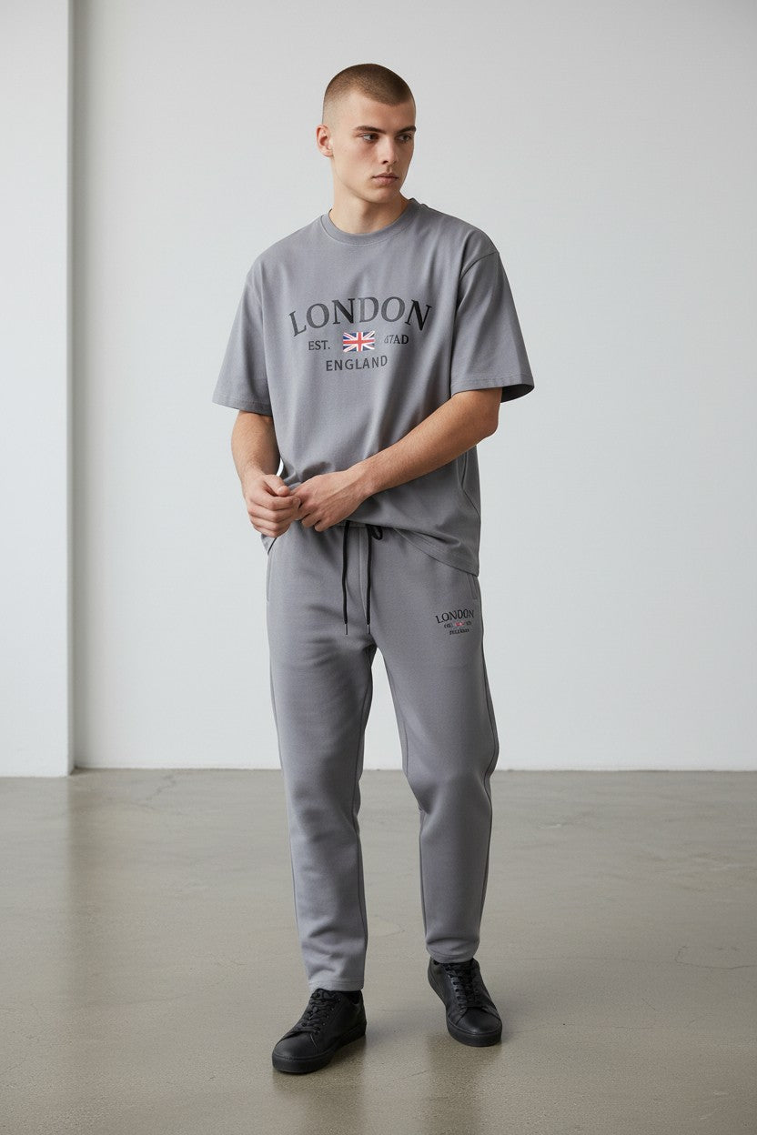 Man wearing a gray London England t-shirt and pants in a minimalistic setting. Antler, Monza Outlet, Monza Fashion, Shein Outlet