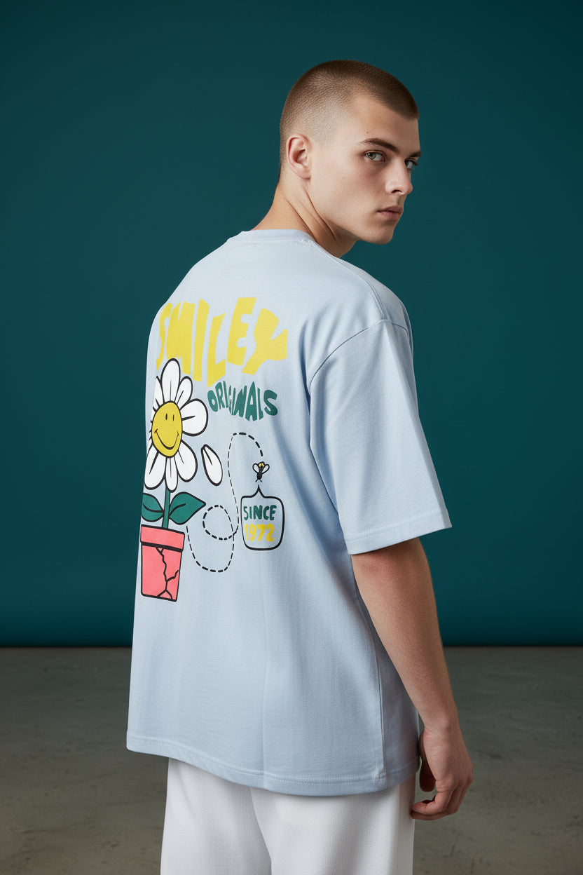 Person wearing a light blue t-shirt with colorful graphics on the back against a teal background. Monza Outlet, Monza Fashion, Shein Outlet