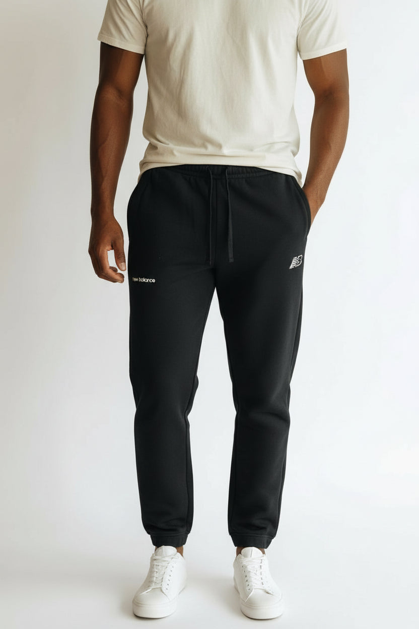 Person wearing black jogger pants with a brand logo on a white background. New Balance, Monza Outlet, Monza Fashion, Shein Outlet