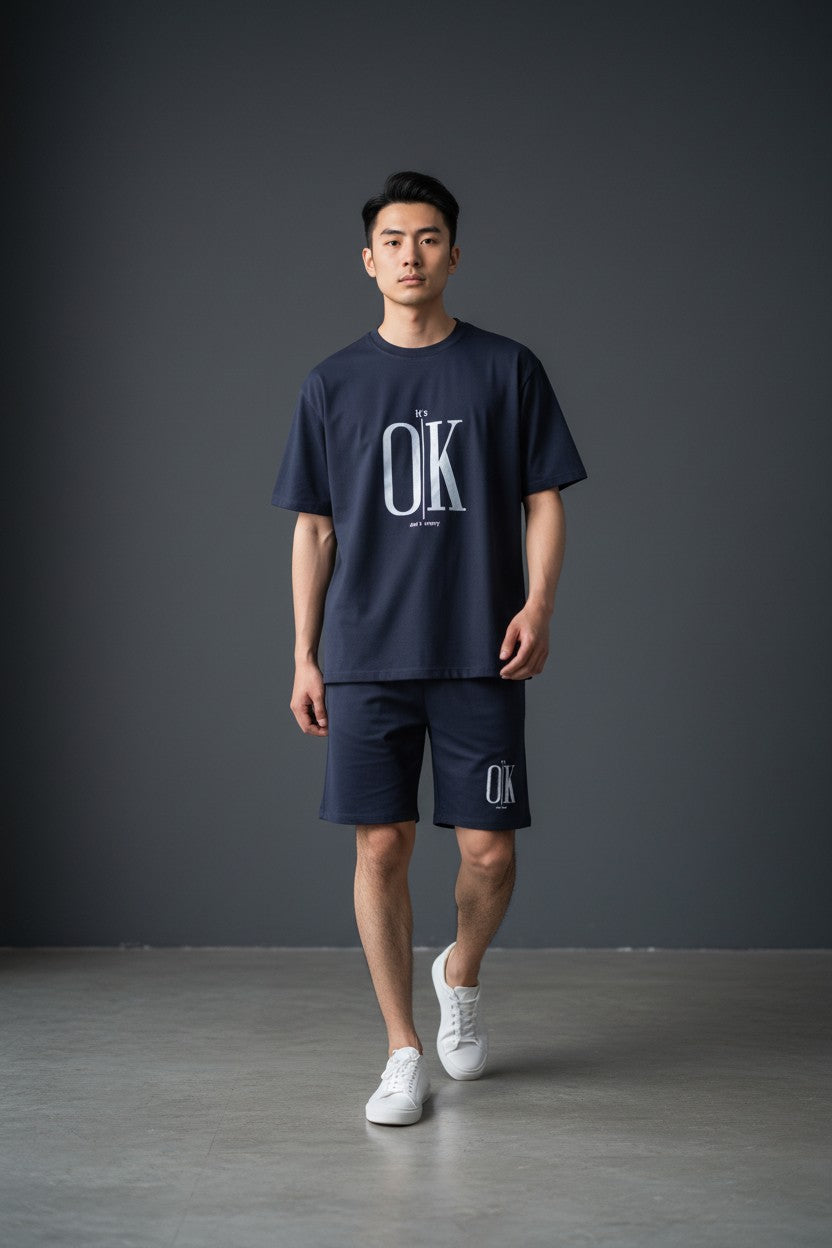 Person wearing a navy blue t-shirt and shorts with OK branding on a gray background. Antler, Monza Outlet, Monza Fashion, Shein Outlet