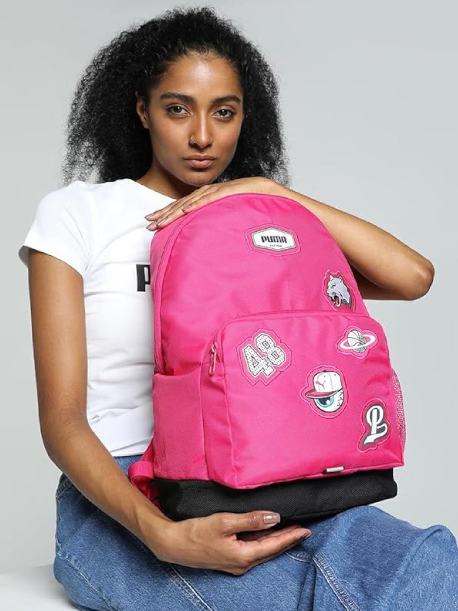 Person wearing a pink backpack with various patches on a gray background. Puma, Monza Outlet, Monza Fashion, Shein Outlet