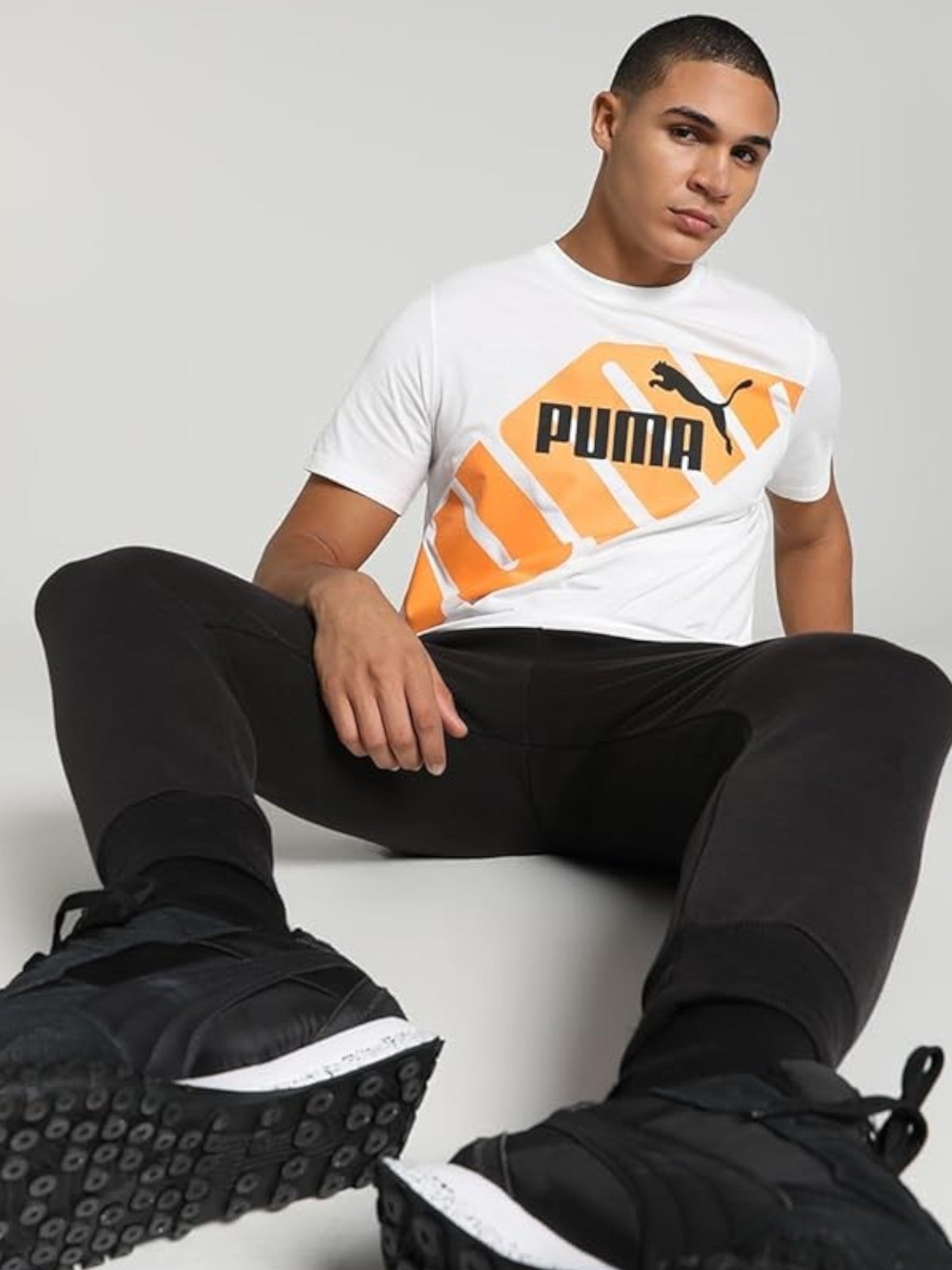 Person wearing a Puma t-shirt and black pants sitting on a white chair.  Puma, Monza Outlet, Monza Fashion, Shein Outlet 