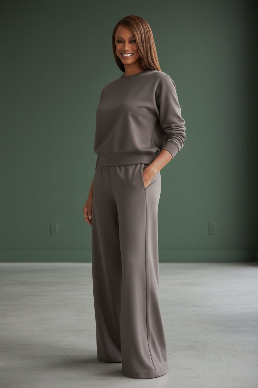 Woman wearing a gray sweater and wide-leg pants against a green wall. Roncato, Monza Outlet, Monza Fashion, Shein Outlet