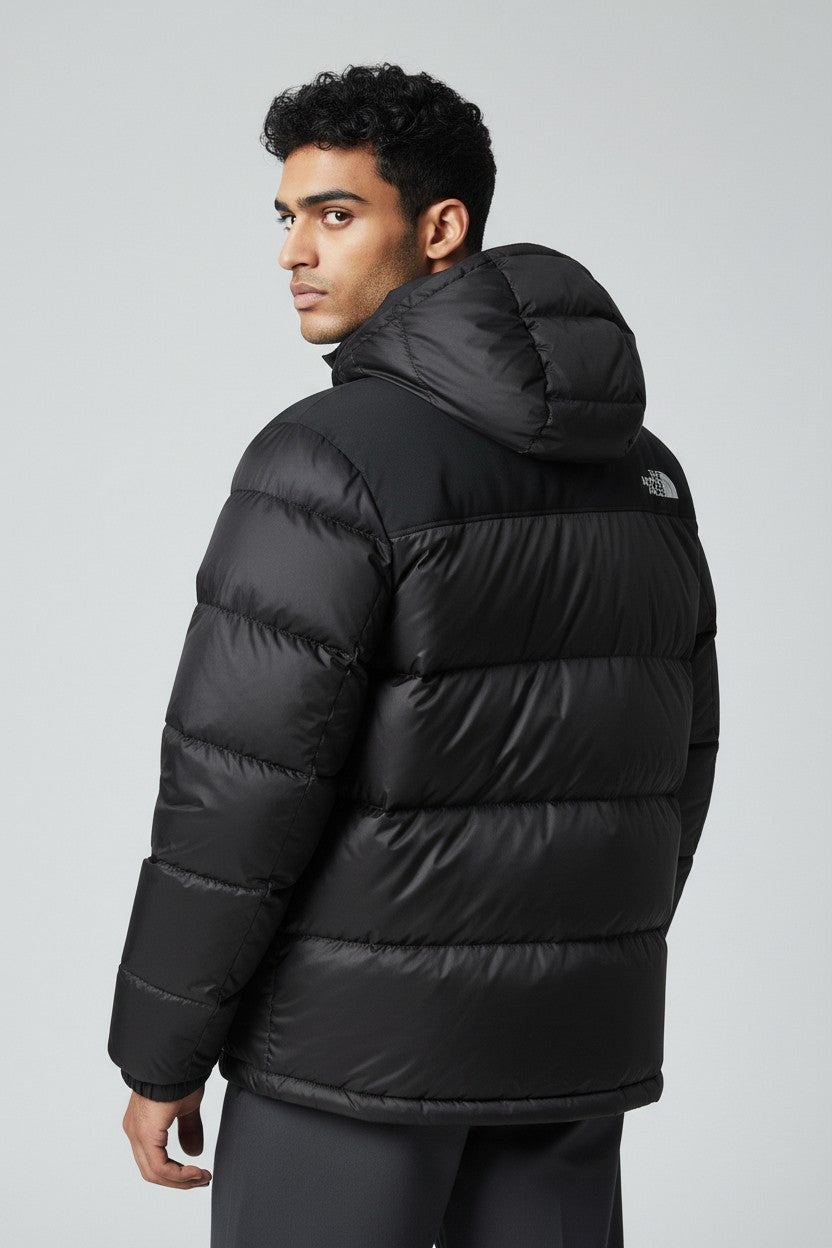 Person wearing a black puffer jacket with The North Face logo on a gray background. The North Face, Monza Outlet, Monza Fashion, Shein Outlet