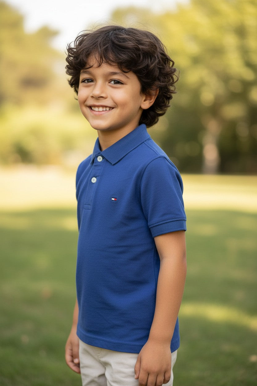 Child wearing a blue polo shirt standing outdoors with greenery in the background. Tommy, Monza Outlet, Monza Fashion, Shein Outlet